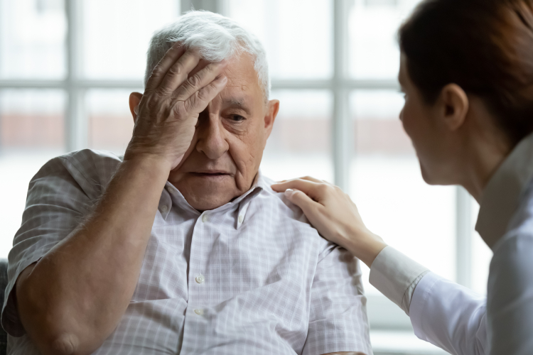 Elderly man holds his head and is comforted