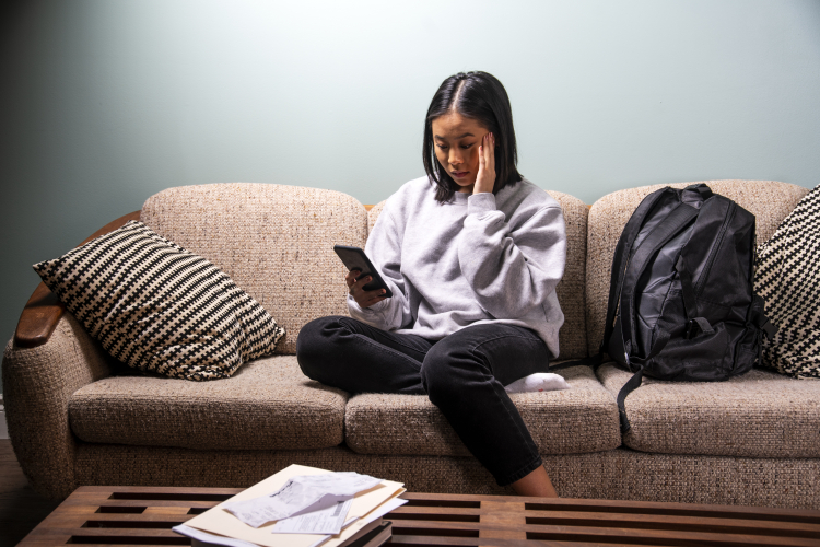 woman sitting on the sofa with her phone out, looking concerned