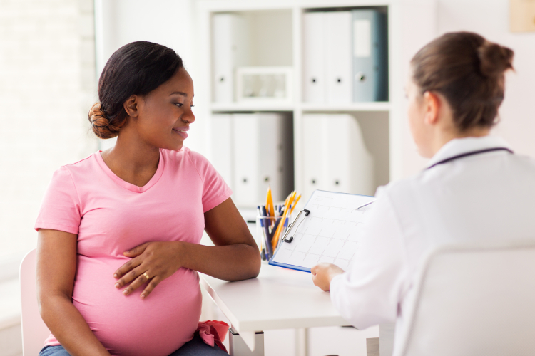 pregnant woman cradling her bump and speaking to a doctor