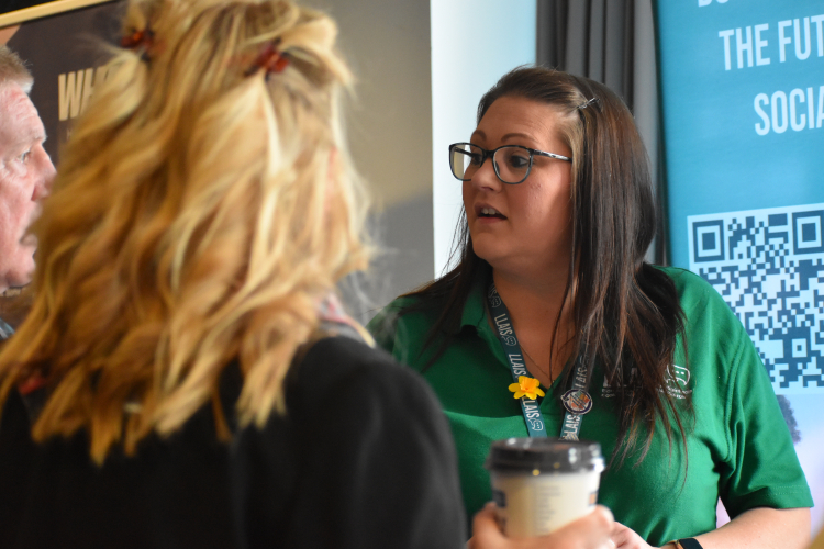 Llais member of staff with green llais polo, engaging with people at a stand